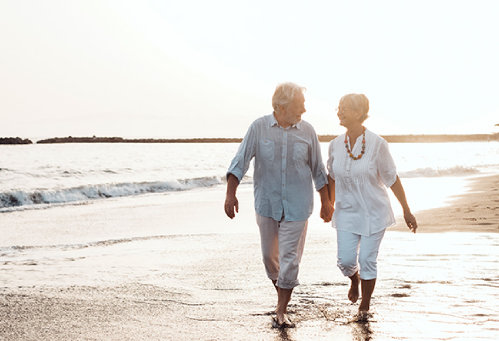 Senior couple holding hands while walking on the beach at sunrise