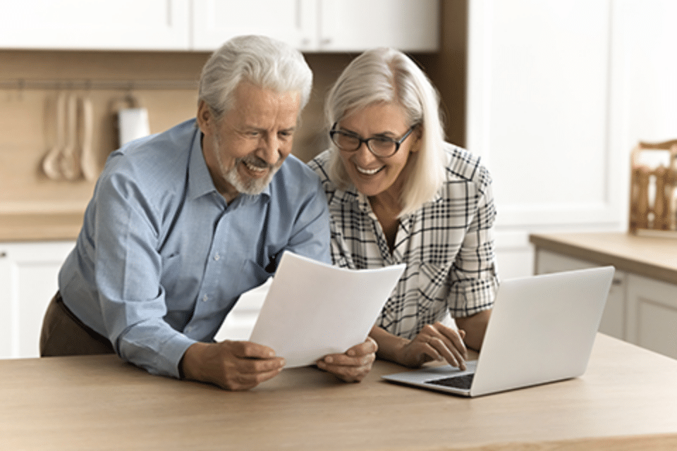 Plymouth Harbor on Sarasota Bay: Senior Couple Leaning on Counter in Kitchen with Laptop Looking at Paperwork