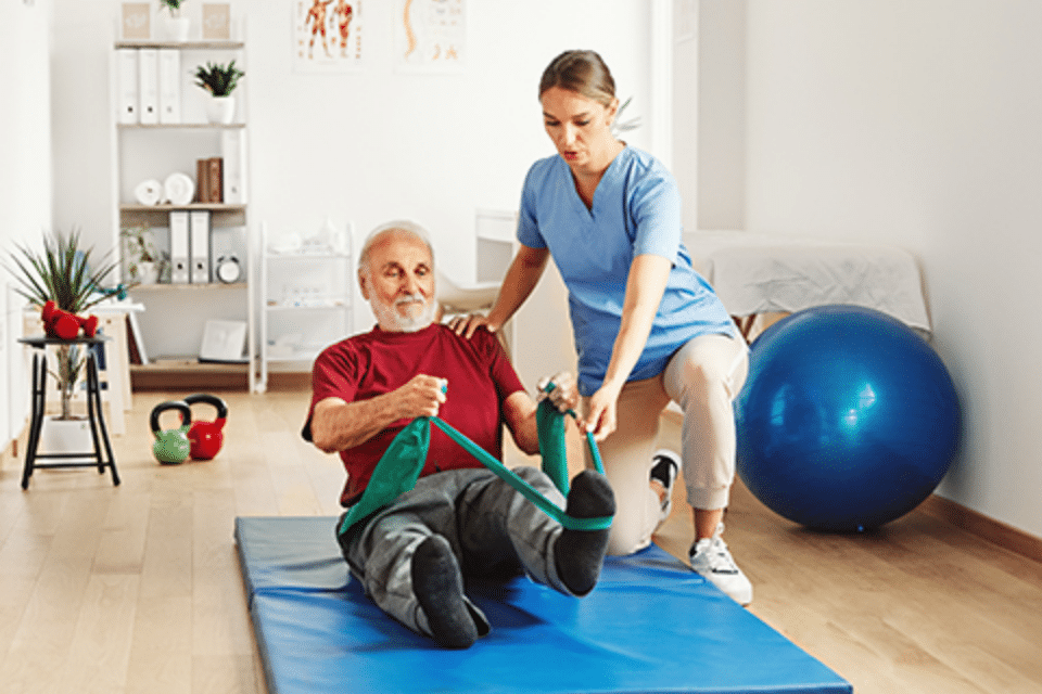 Plymouth Harbor on Sarasota Bay: Caregiver Helping Senior with Exercise Band While Seated on a Mat on the Floor