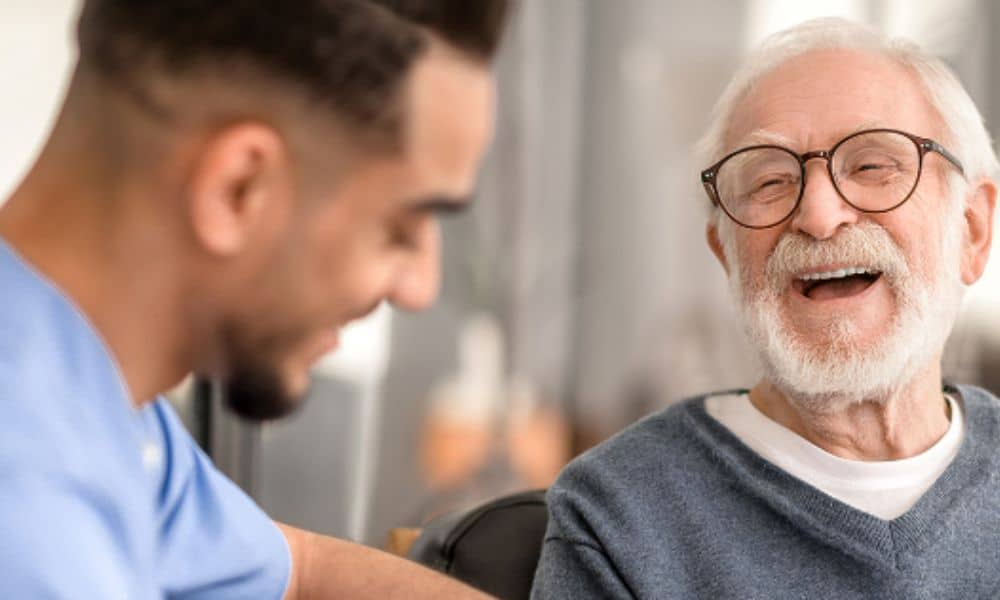A smiling elderly man engages in conversation with a caring nurse.