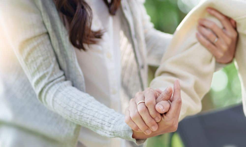 A woman gently holds the hand of an elderly man.