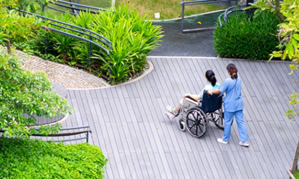 A nurse gently pushes a wheelchair along a deck toward a path.