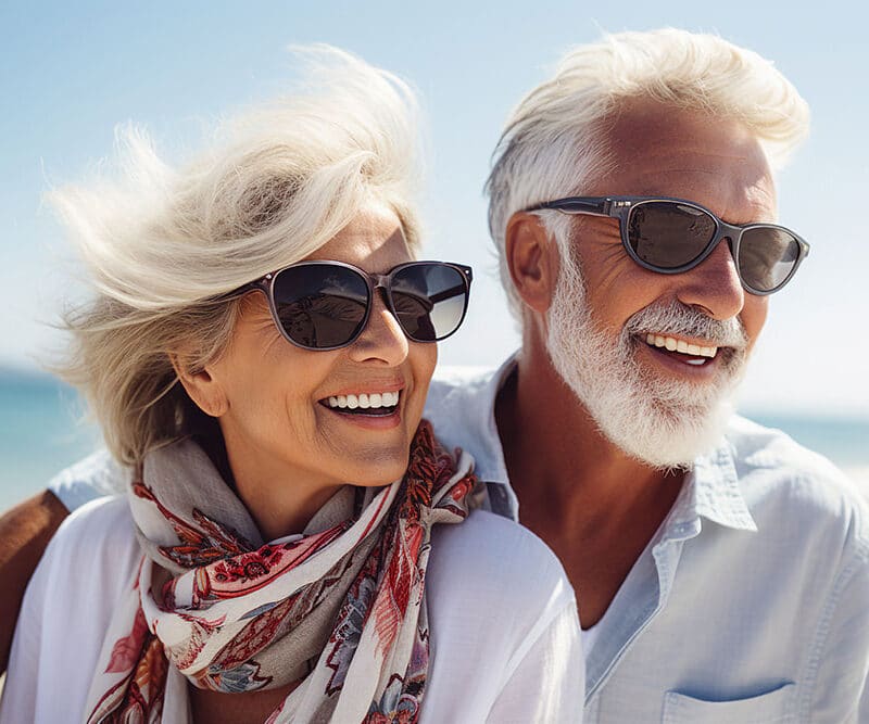 An older couple wearing sunglasses enjoys a sunny day at the beach