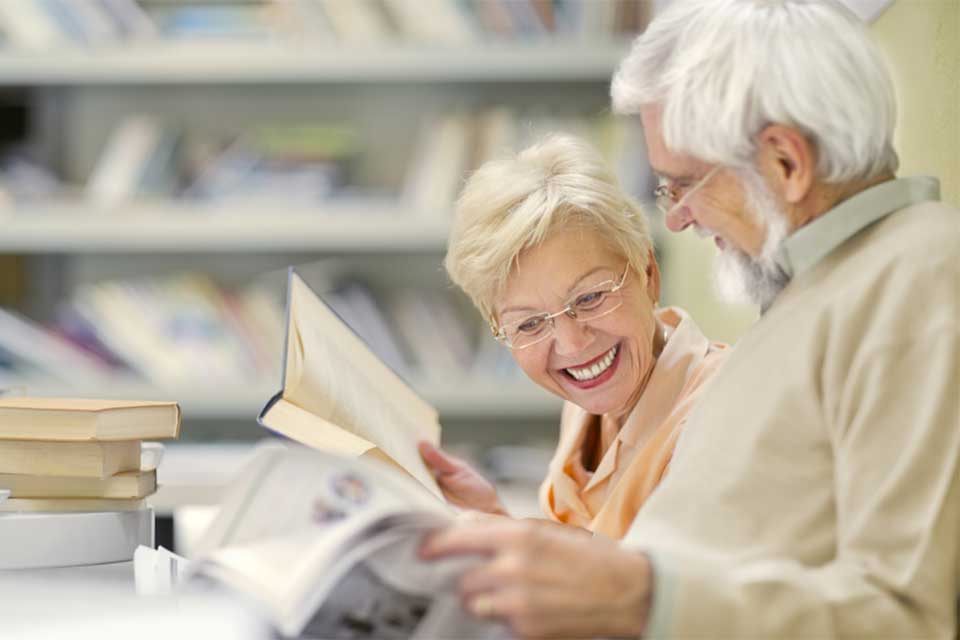 An older couple sits together, looking at a book, smiling.