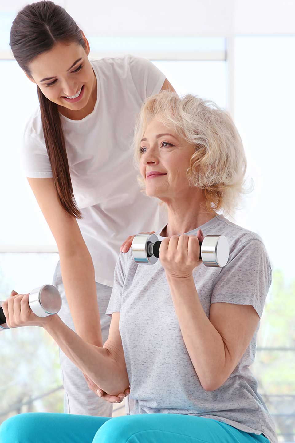 A woman assists an older woman in lifting dumbbells during a workout session