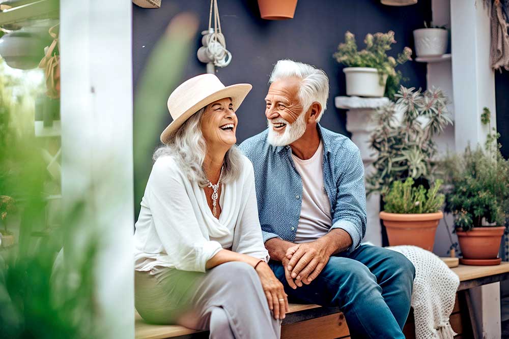 A senior couple sitting on a bench outside laughing