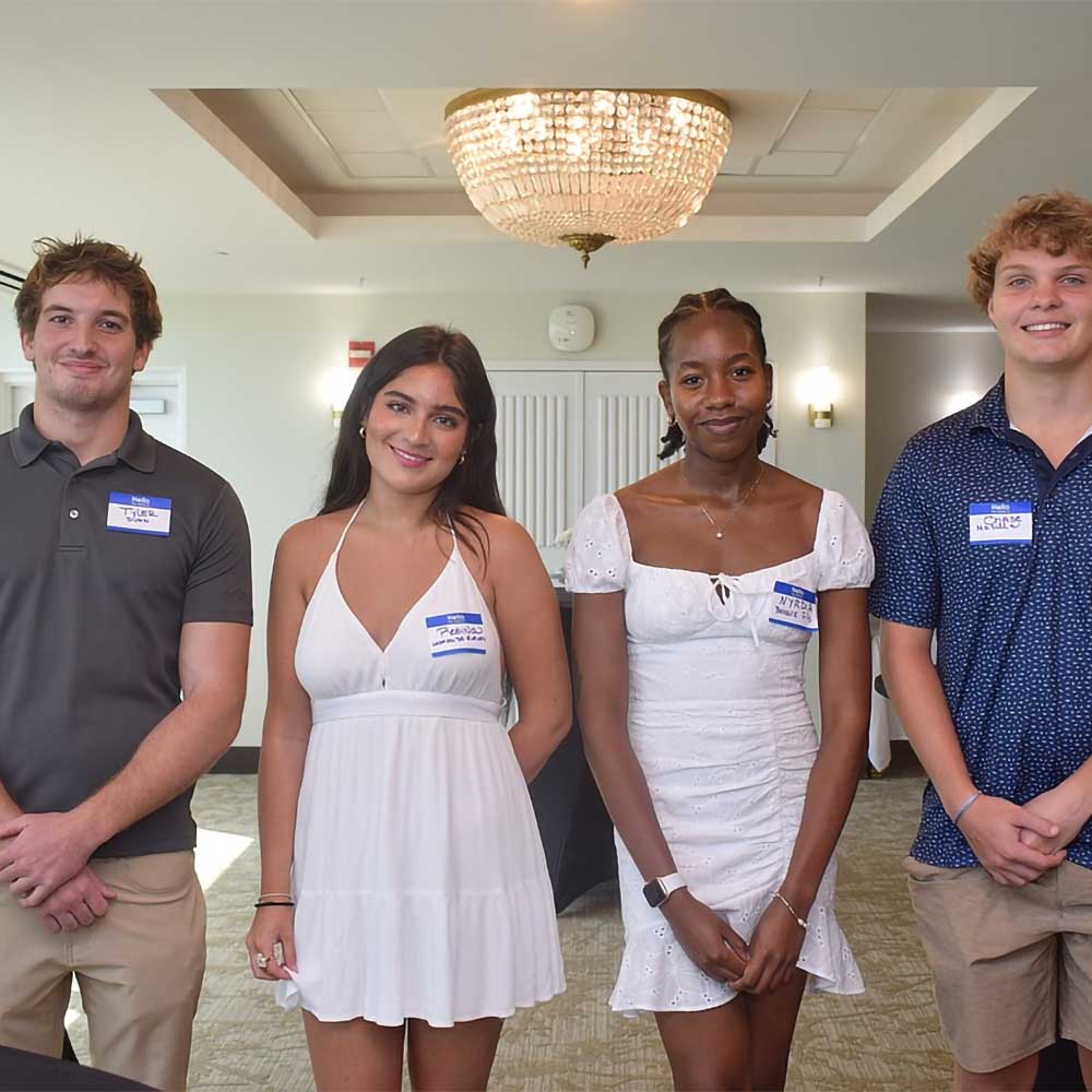 Four young people, recipients of Plymouth Harbor scholarships, pose in a room, smiling.