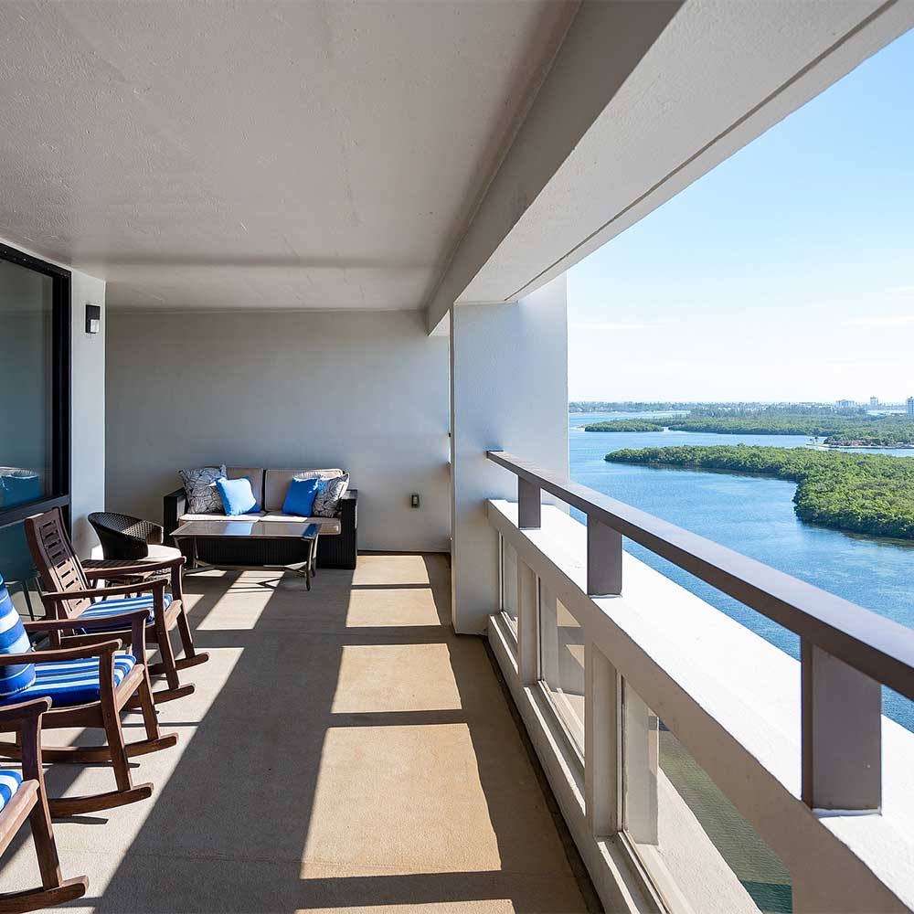 A balcony with chairs overlooks Plymouth Harbor and the serene waters of Sarasota Bay.