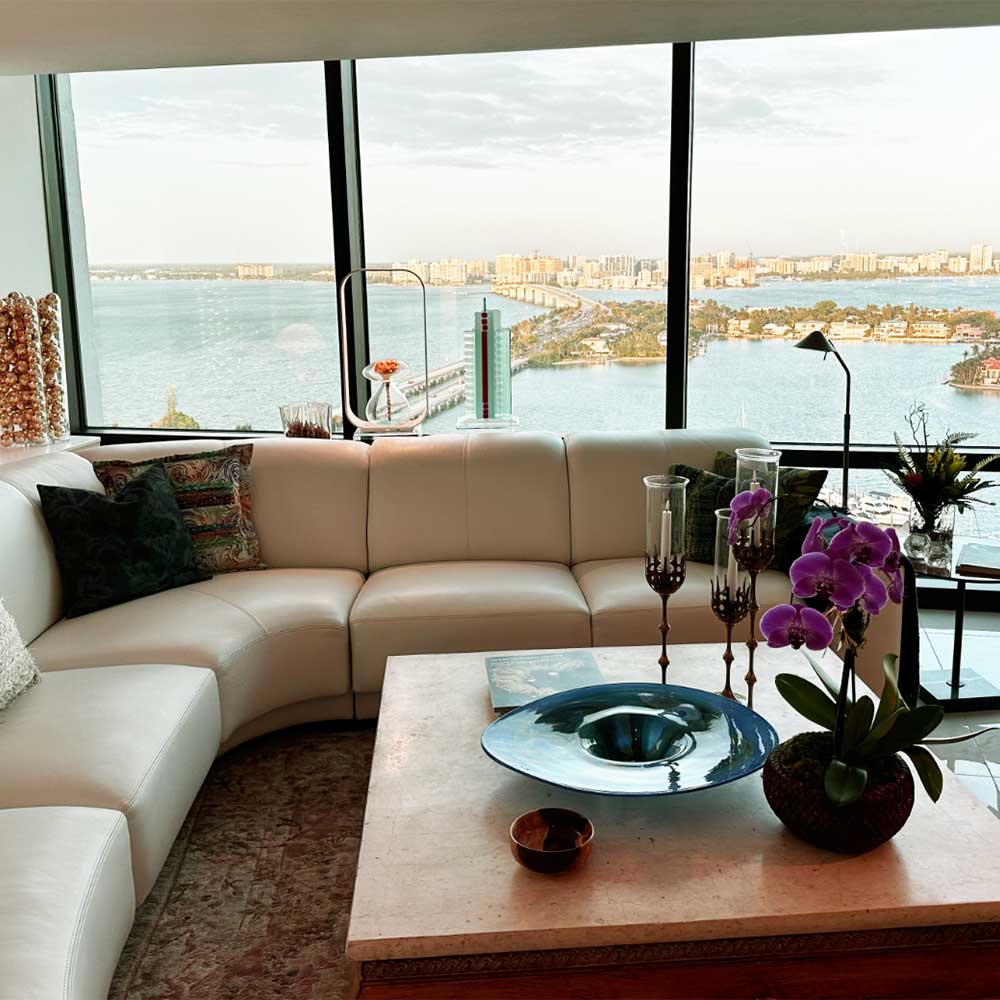 Inviting living room with expansive windows offering a picturesque view of Sarasota Bay from Plymouth Harbor's independent living space.