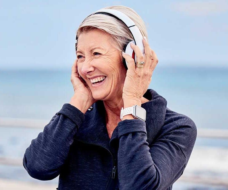 A senior woman standing on the beach listening to music on her headphones