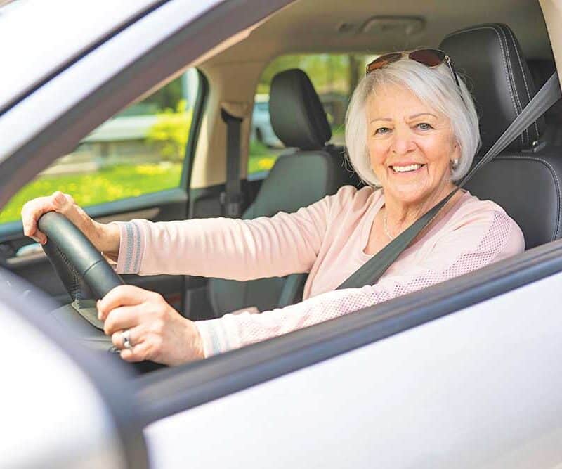 A senior woman sitting in the driver's seat of a car