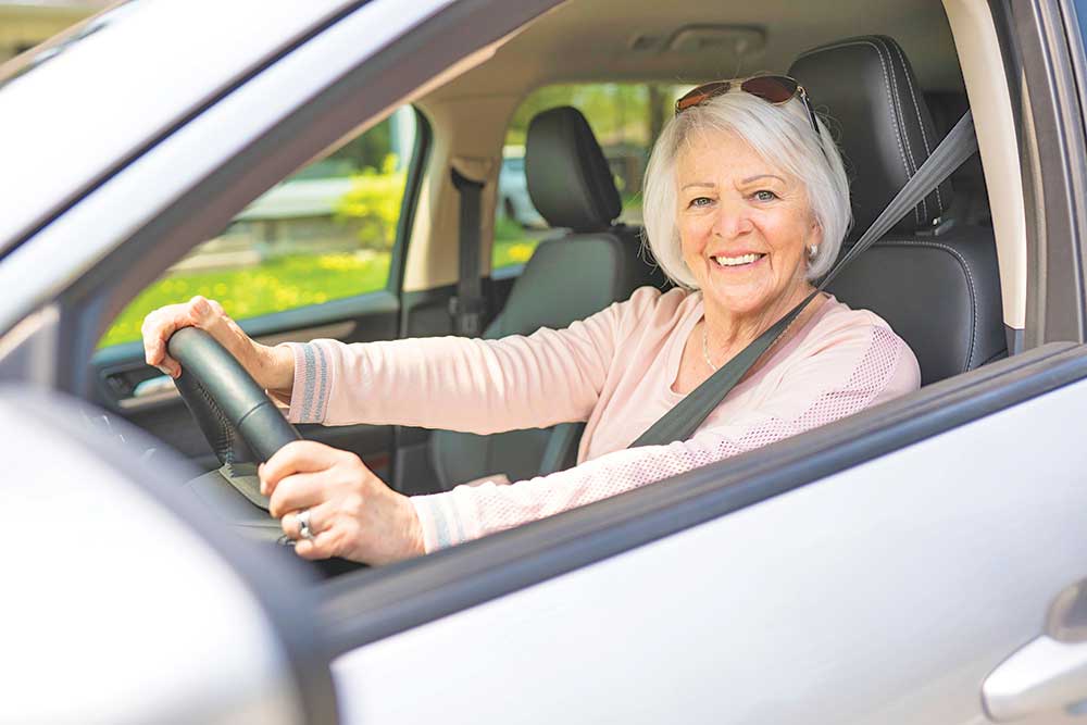 A senior woman sitting in the driver's seat of a car