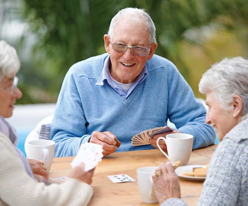 Two senior women and one senior man seated at a table playing a card game