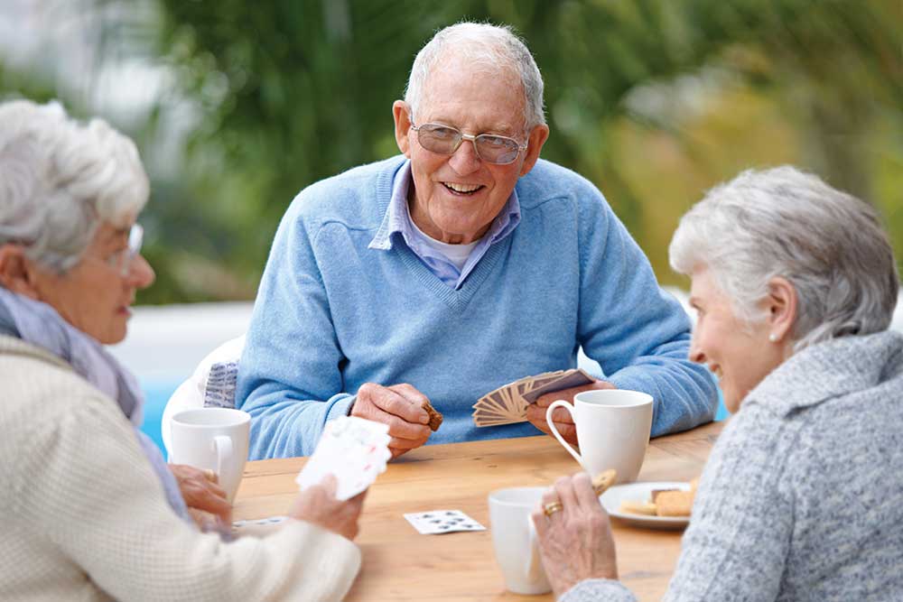 Two senior women and one senior man seated at a table playing a card game