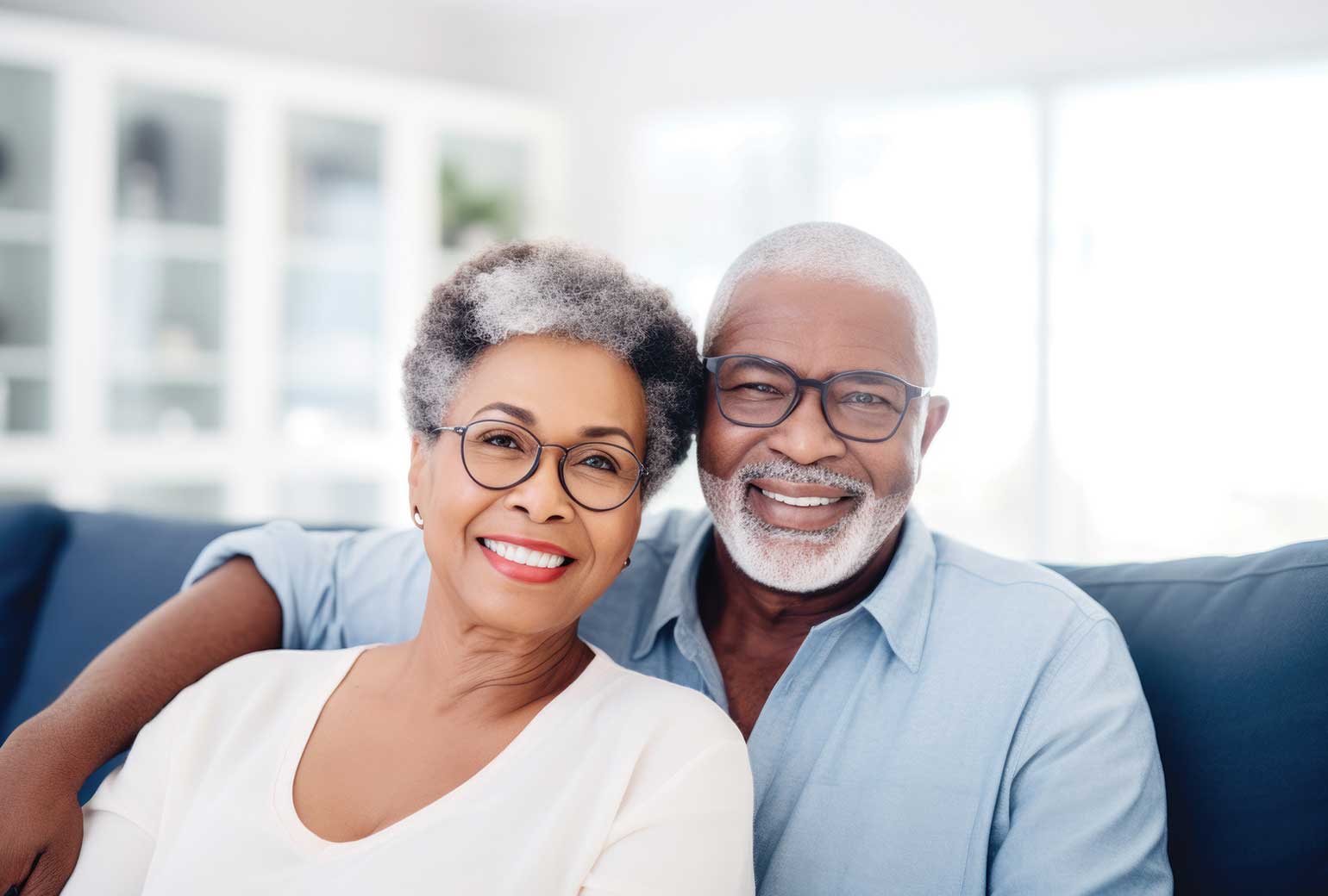 An older couple smiles while sitting together on a cozy couch, enjoying each other's company in a warm living room.