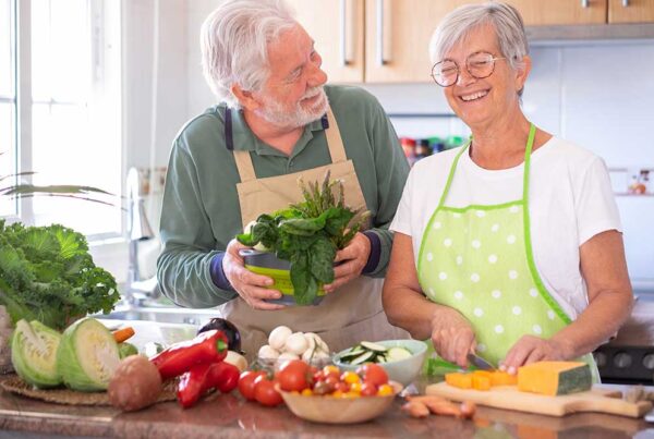 Senior man and woman stand at kitchen counter preparing vegetables