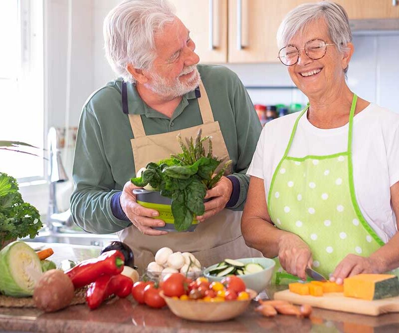 Senior man and woman stand at kitchen counter preparing vegetables