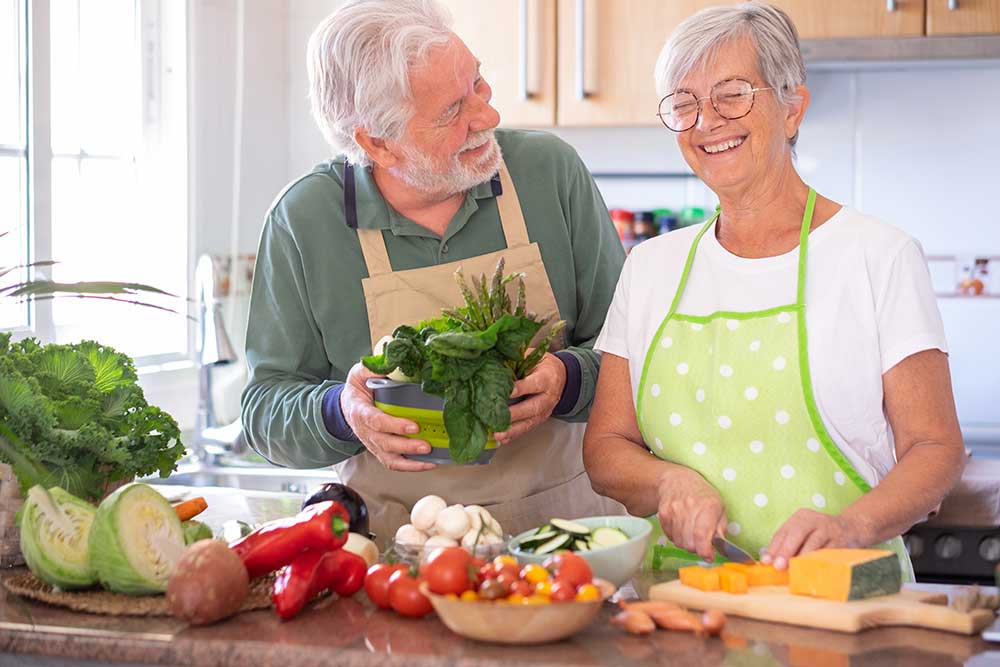 Senior man and woman stand at kitchen counter preparing vegetables